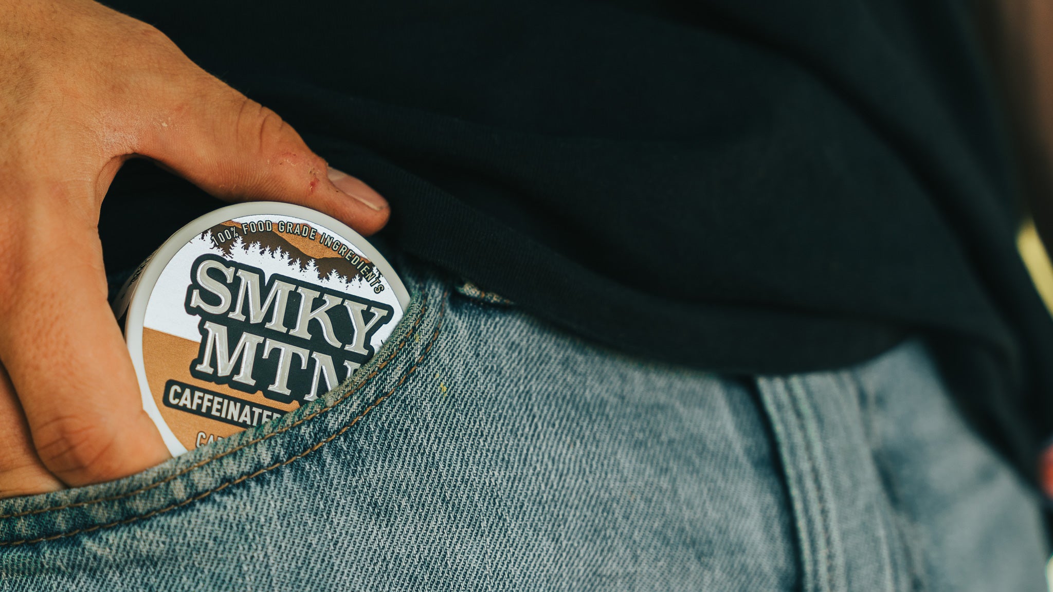 A man pulling a can of smokey mountain caramel coffee flavored caffeinated pouches out of the front pocket of his blue jeans.