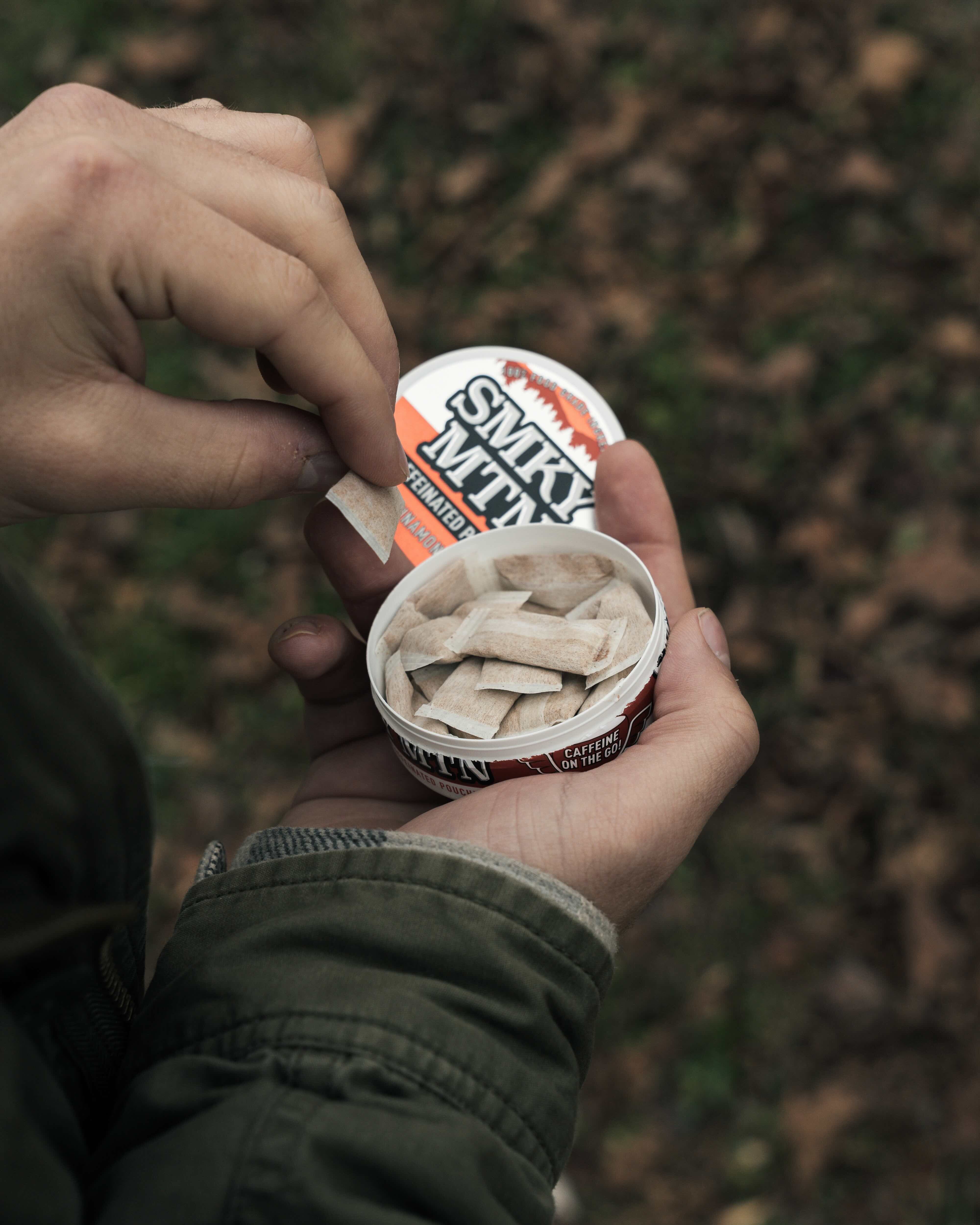 Hand pulling Smokey Mountain Cinnamon Fire Caffeinated Pouches from the can