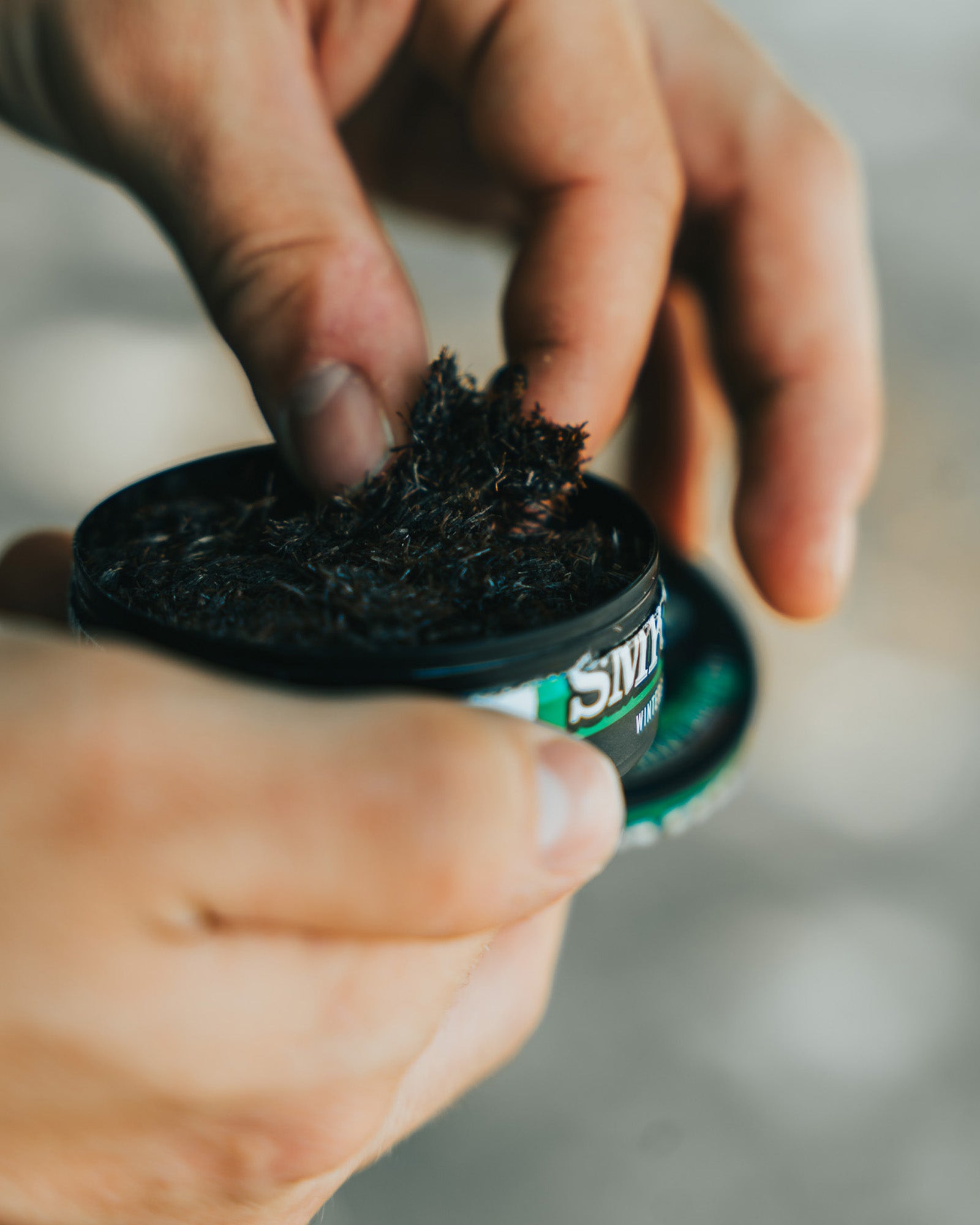 A hand pulling a pinch of smokey mountain wintergreen long cut out of a can.